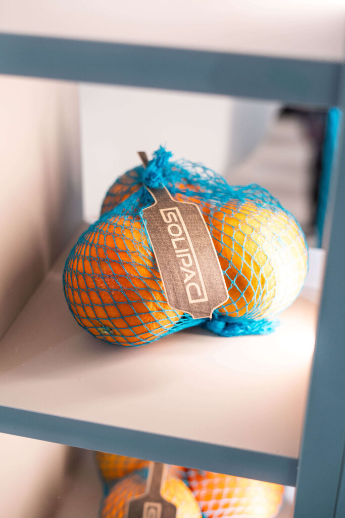 Orangen in türkisem Solipac Raschelnetz mit Stegetikett – atmungsaktive Netzverpackung für frisches Obst im Einzelhandel.